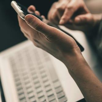 Person messaging their attorney from a phone while working at a laptop